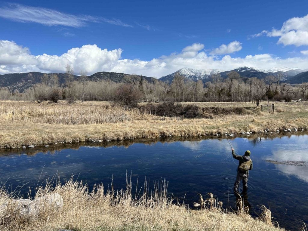 a person fly fishing while wading knee deep in a river near bozeman