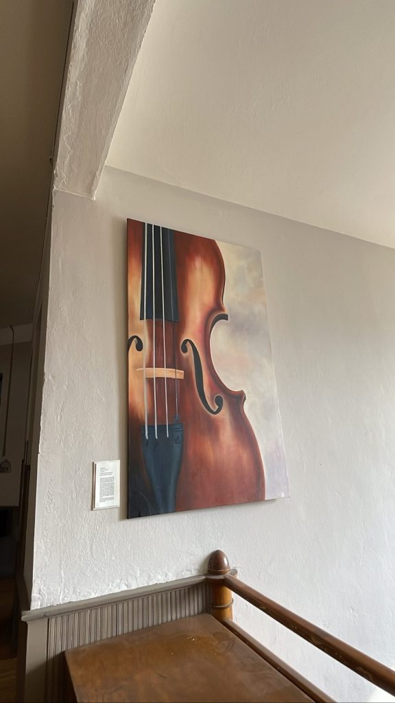 Painting of a cello displayed on a wall inside of the Livingston center for art and culture