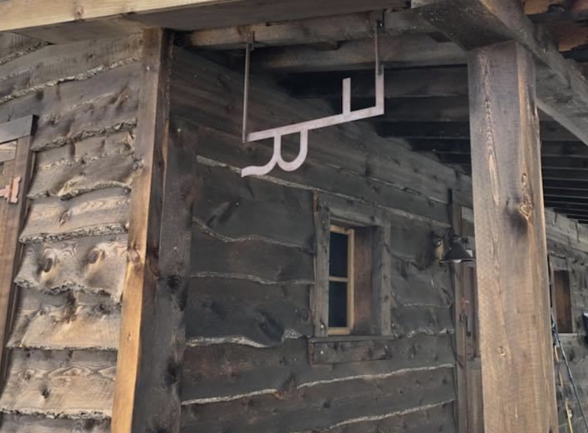 a metal sign hangs from the covered porch of a log building at the crail ranch homestead 