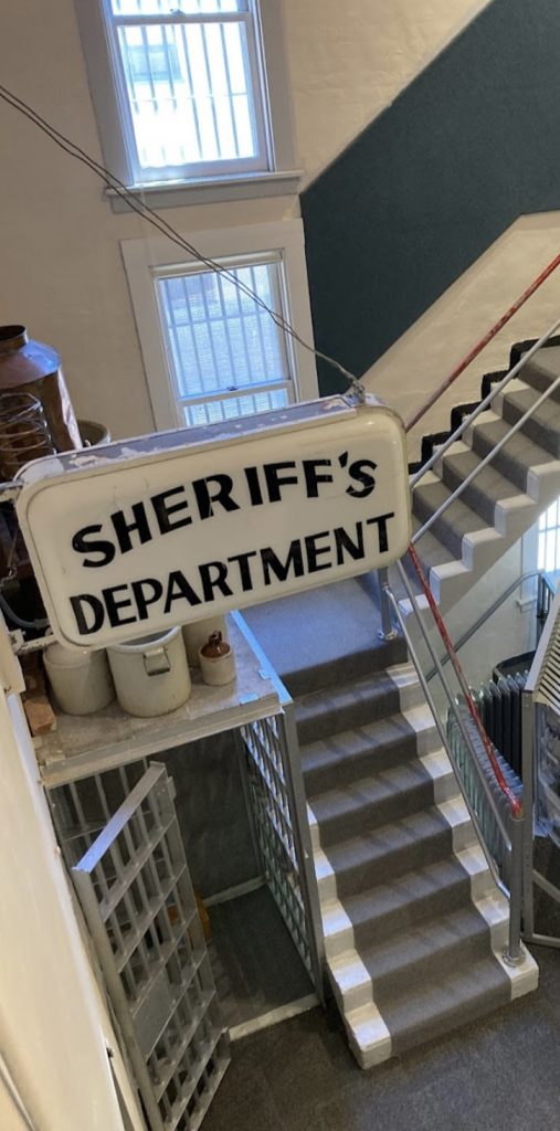 a sign saying 'sheriff's department' is hung above a jail cell and stairway, displayed inside the gallatin history museum.