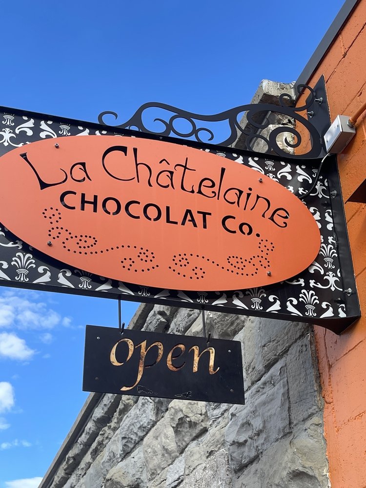 Outside hanging sign for La Chatalaine chocolate Co. with additional signage underneath that says open